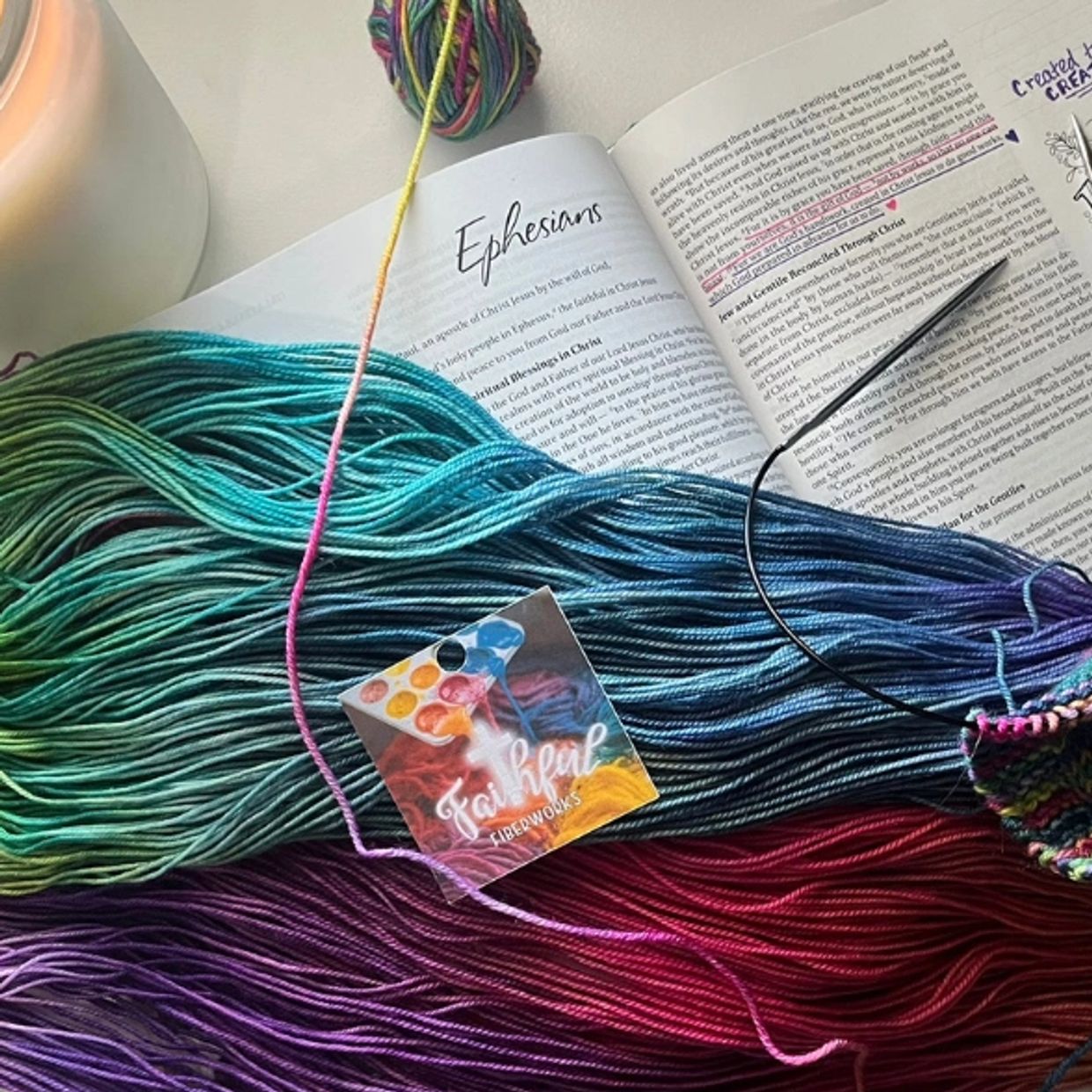 Promise in Every Hue, gauge swatch in progress, lit candle, and an open Bible on Ephesians.
