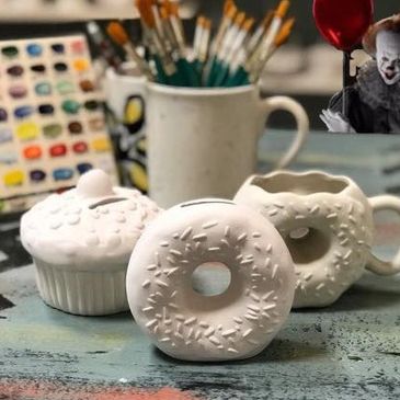 White ceramic donut, cupcake, and cup on a rustic table with paintbrushes in the background.