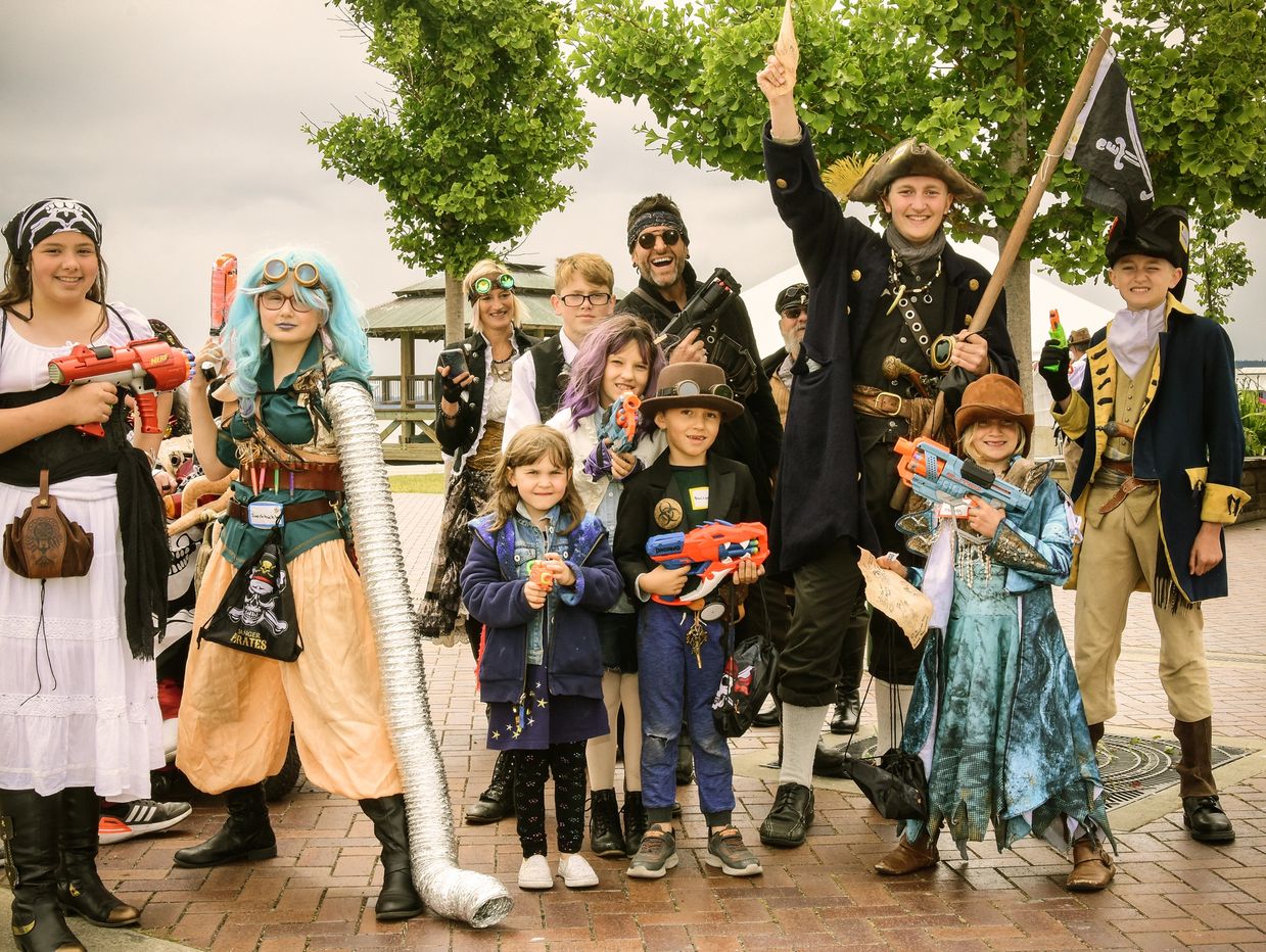 Group of people in pirate and steampunk costumes holding toy guns and posing outdoors.