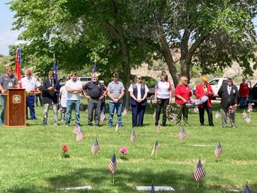 Veterans and community members gather in a cemetery for a memorial event with American flags.
