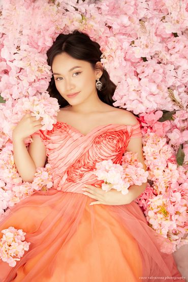 Young woman in a coral dress surrounded by pink flowers.