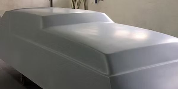 A covered vehicle shape under a smooth white cover indoors.