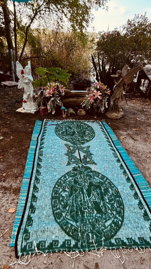 Outdoor memorial with statues, flowers, and a woven rug.