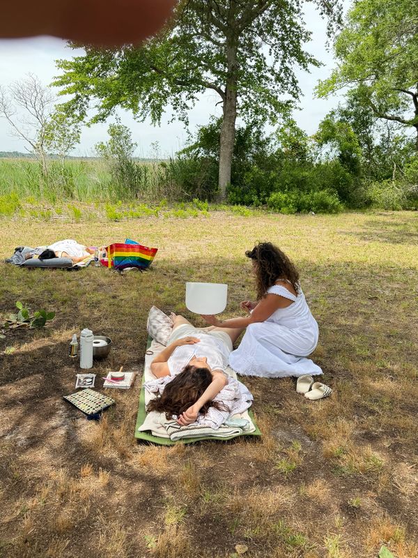 Two women in white dresses relax outdoors with nature surrounding them.