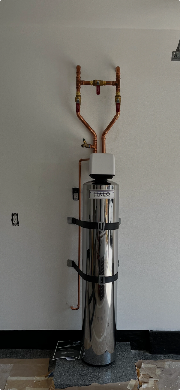 A shiny Halo water softener installed against a wall with copper piping.