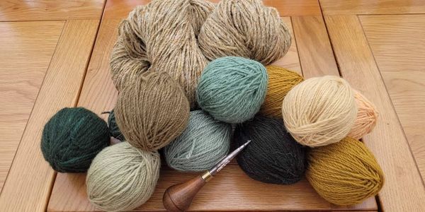 A pile of multicoloured rough wool balls sit atop a wooden table with a needle punch tool