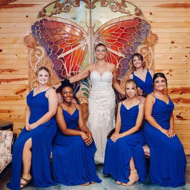 A bride in a white dress flanked by bridesmaids in blue dresses against a wooden butterfly backdrop.