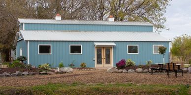Blue single-story horse barn with a metal roof and landscaped garden in front.
