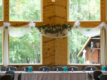 Elegant dining hall with large windows, chandelier, and decorated tables ready for an event.