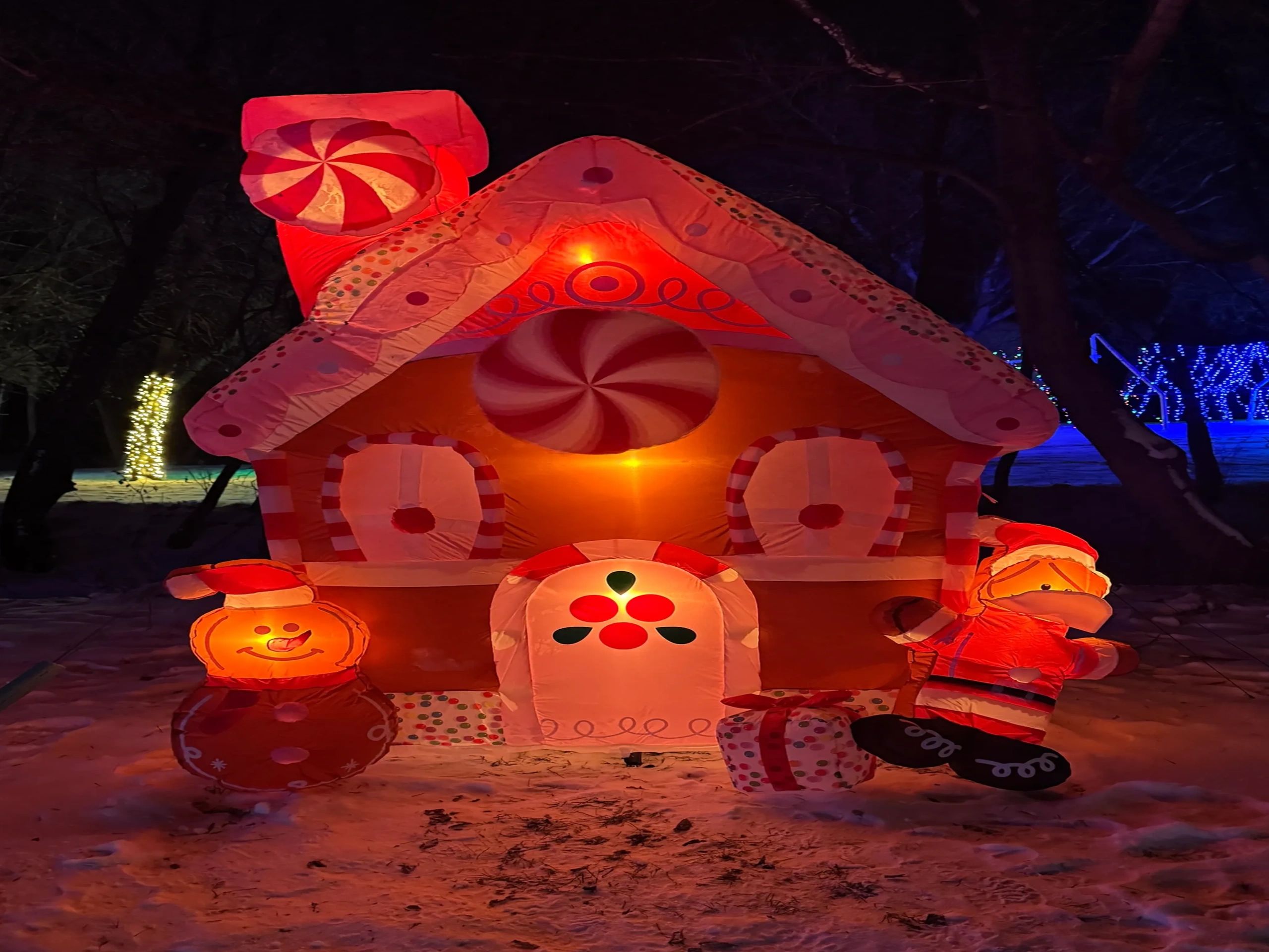 Large inflatable gingerbread house with Christmas characters in a snowy wooded display