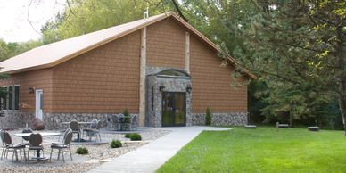 Wooden building with stone accents surrounded by greenery and outdoor seating.