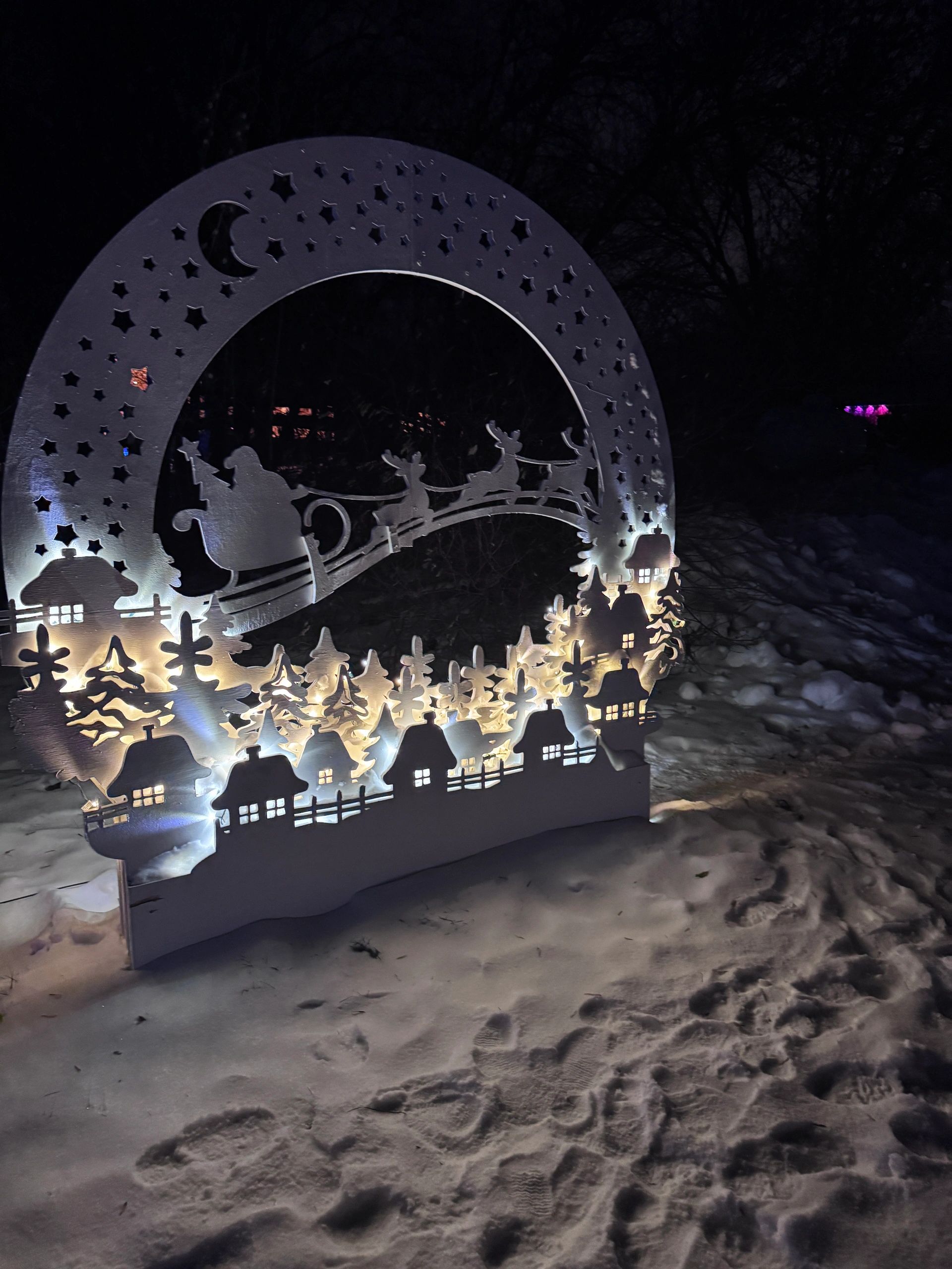 Illuminated wood Christmas scene showing Santa and reindeer flying over a snowy village