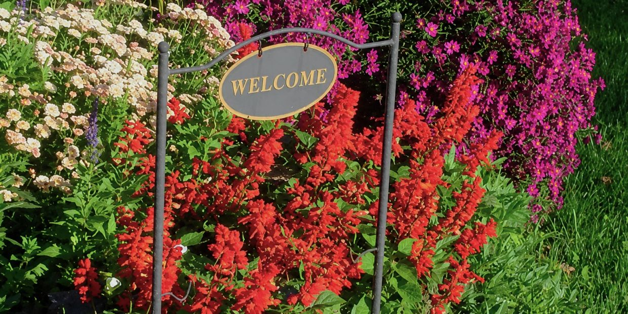 A garden with colorful flowers and a 'WELCOME' sign.