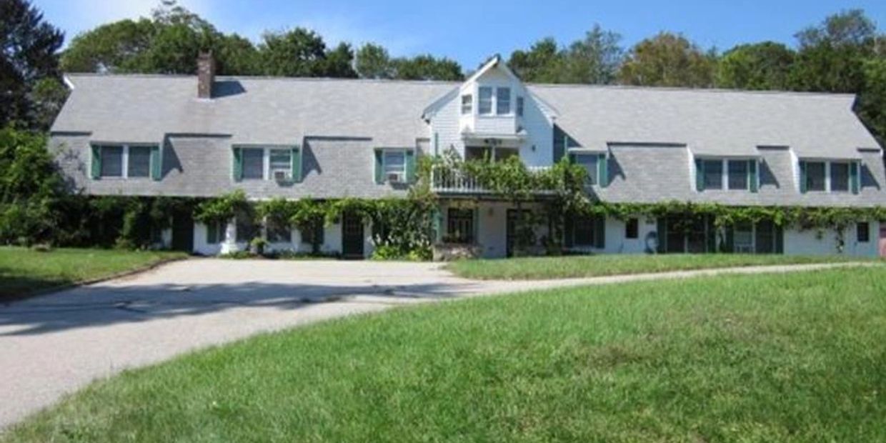 Large white house with greenery and a long driveway.