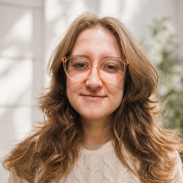 Young woman with glasses and wavy hair smiling gently.