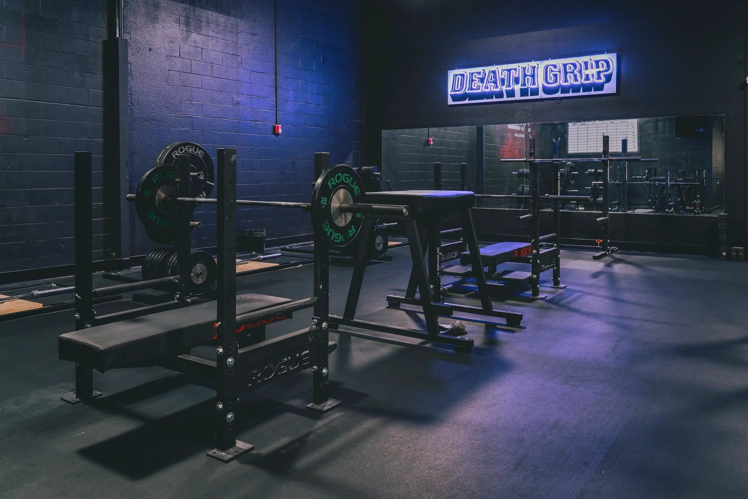 Weightlifting gym with benches and weights under a neon "DEATH GRIP" sign.