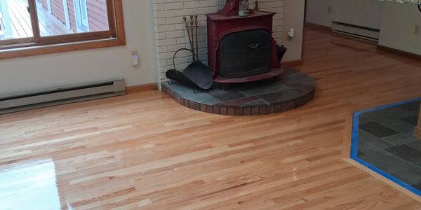 Polished hardwood floor with a red wood stove and large window.