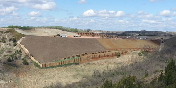 Large earthwork dam under construction with heavy machinery on top.