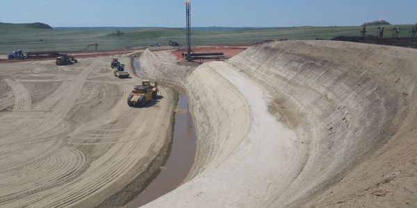 Heavy machinery working on a large earth excavation site with a gas flare in the background.