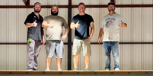 Four men standing on a platform giving thumbs up.