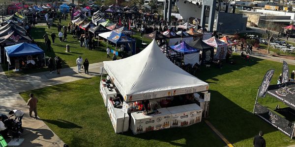 Outdoor market with multiple vendor tents on grass.