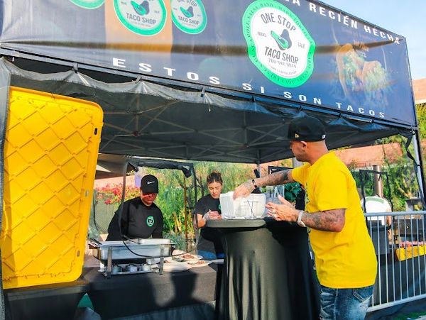 People at a taco shop booth outdoors.