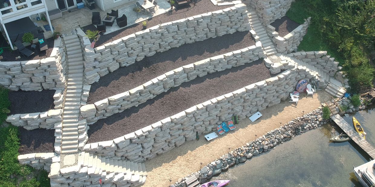 Terraced stone retaining walls with stairs leading to a lakeside sandy beach area.