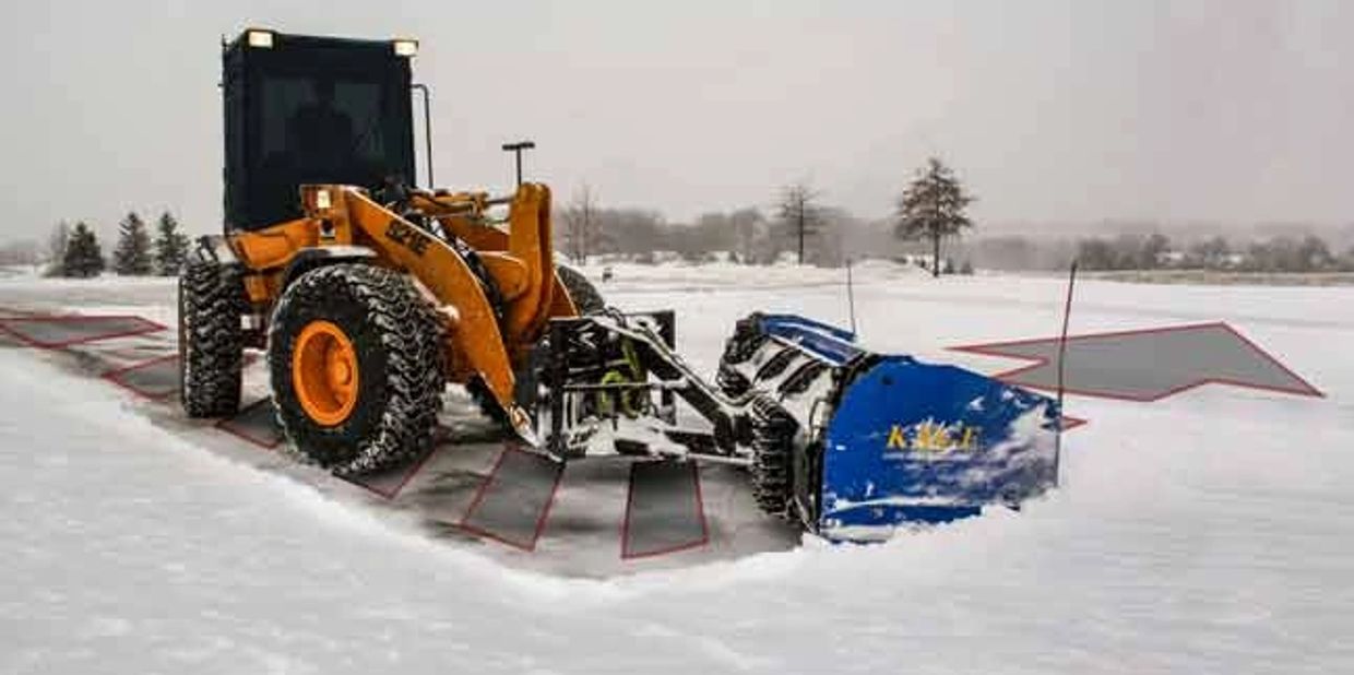 A yellow snowplow clearing snow with marked areas in a snowy landscape.