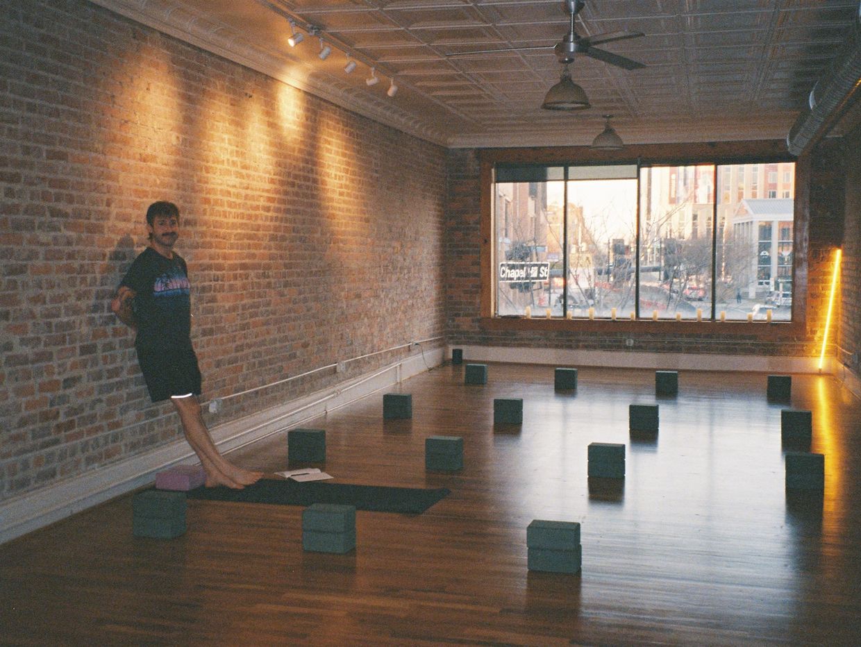 Man standing on yoga mat in a spacious studio with brick walls and city view.