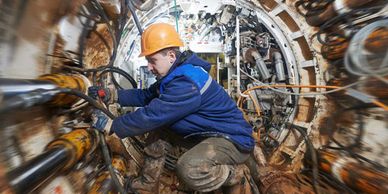 Worker in protective gear operating machinery inside a confined industrial space.