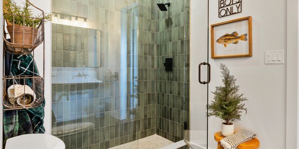 Modern bathroom with green tiled shower and hexagonal floor tiles.