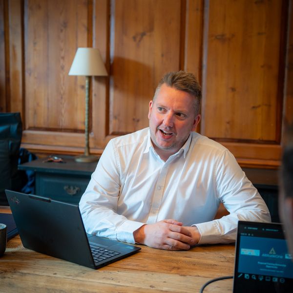 Steve in a white shirt speaking during a meeting with laptops on the table.