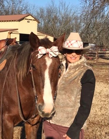 Woman in a cowboy hat posing with a horse wearing a matching bow.