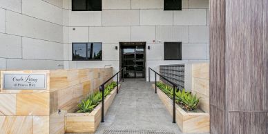 Modern building entrance with stone walls and plants along the walkway.