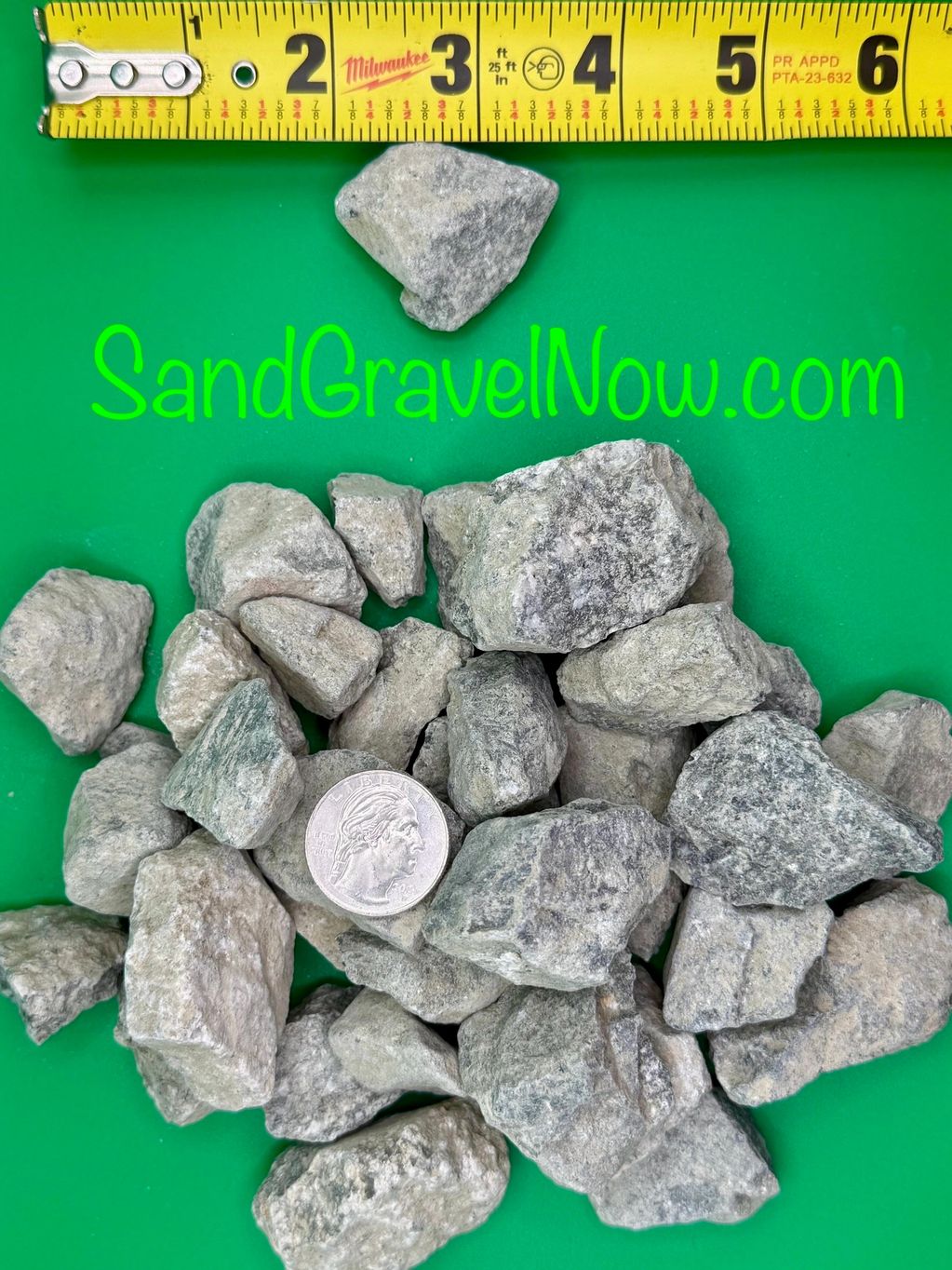 Gray gravel stones with a quarter and measuring tape on green background.