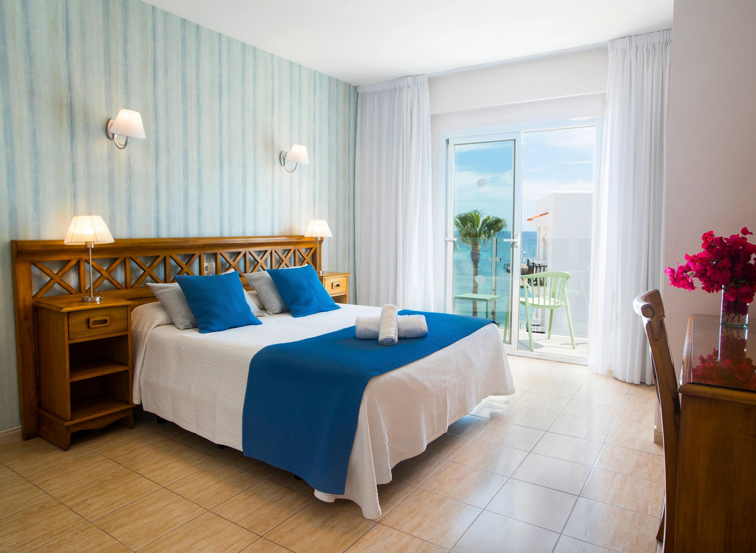 Bright hotel room with blue accents and sea view balcony.