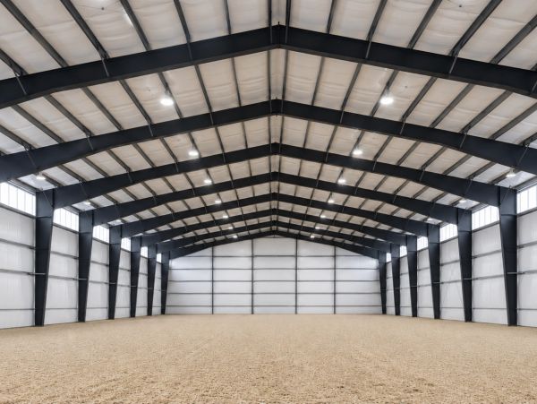 Spacious empty indoor arena with high ceiling and gravel floor.