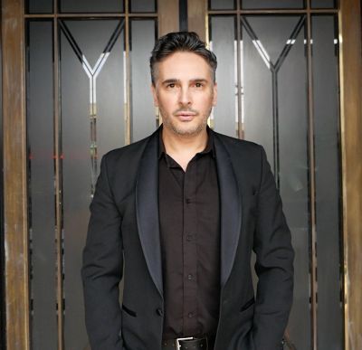 Man in black suit facing the camera confidently.