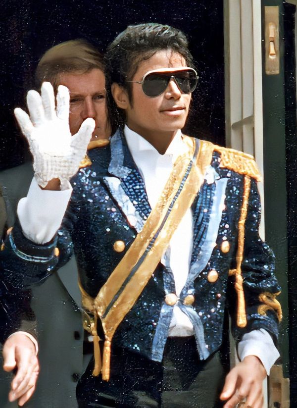 Michael Jackson in a sequined military-style jacket waving with a white glove.
