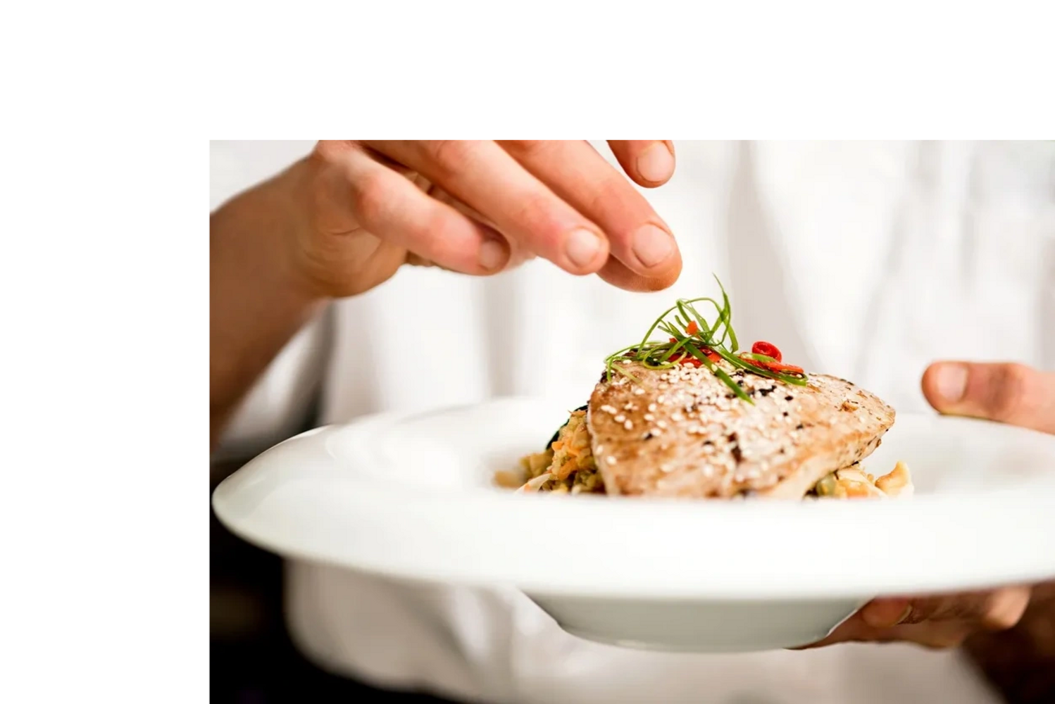 Chef garnishing a plated mahi mahi with herbs and spices.
