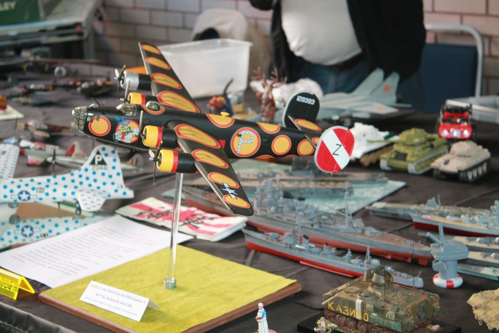 Colorful model airplane and military vehicles on display at a hobby exhibit.