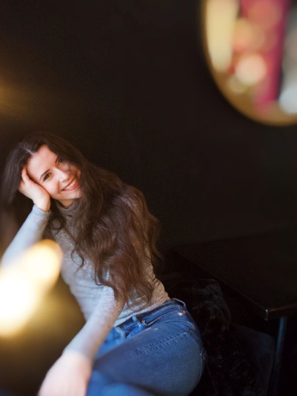 A smiling woman with long hair leaning her head on her hand.