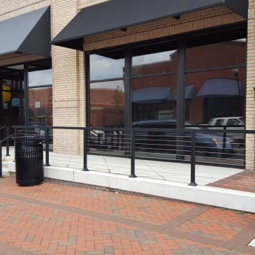 Empty outdoor patio area with metal railing and brick sidewalk.