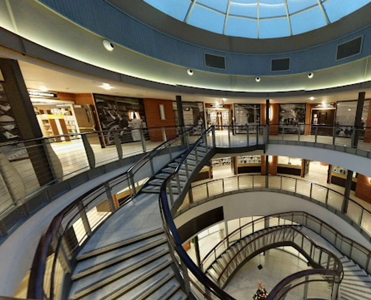 Spiral staircase under a glass dome ceiling in a modern building.