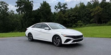 White sedan parked on pavement near grass and trees.