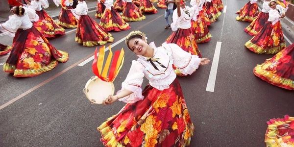 Women in vibrant traditional dresses perform a lively street dance with tambourines.