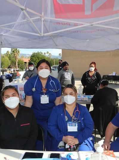 Healthcare workers wearing masks at an outdoor health event under a tent.