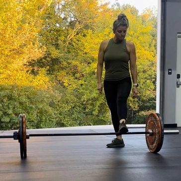 Woman preparing to lift a barbell in a gym with a nature backdrop.