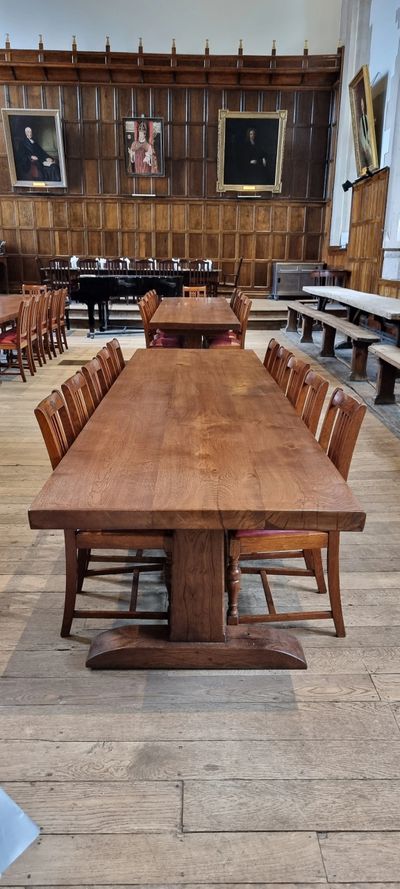 Historic dining hall with long wooden tables and portraits on paneled walls.