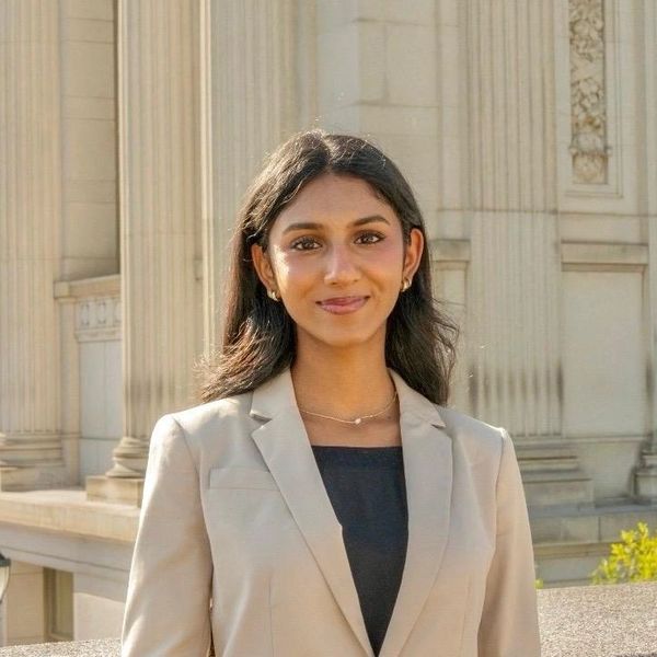 Young professional woman in beige blazer smiling outdoors with classical architecture background.